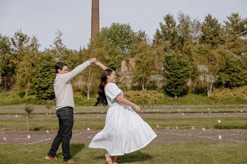A couple dances together on a lawn with a brick building and tall chimney visible in the background.