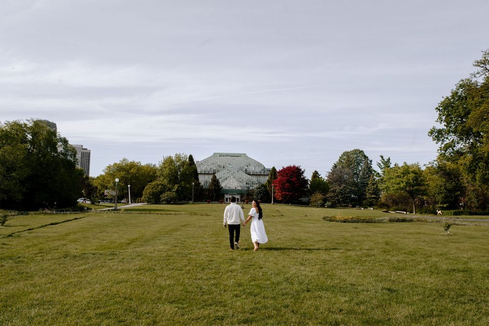 Couple walking hand in hand on grassy hillside during cloudy autumn day.