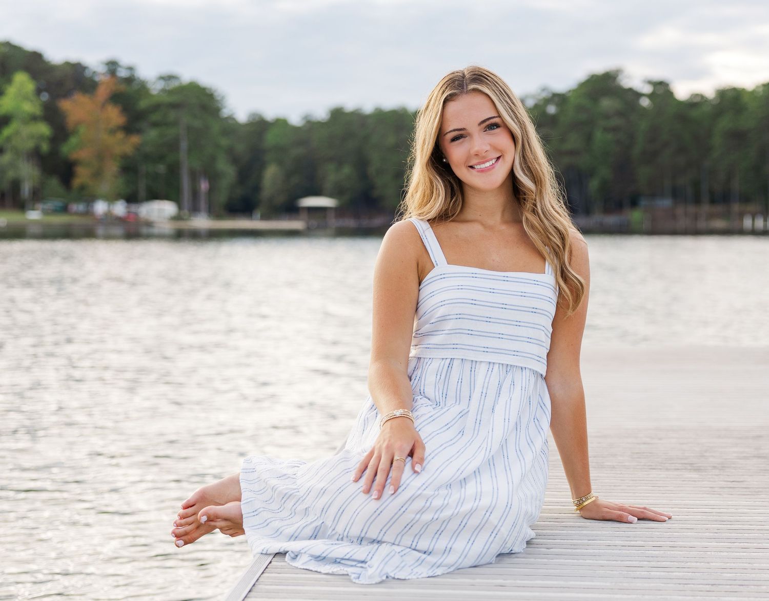 White and blue striped summer dress look on a wooden dock with peaceful lake and trees in background.