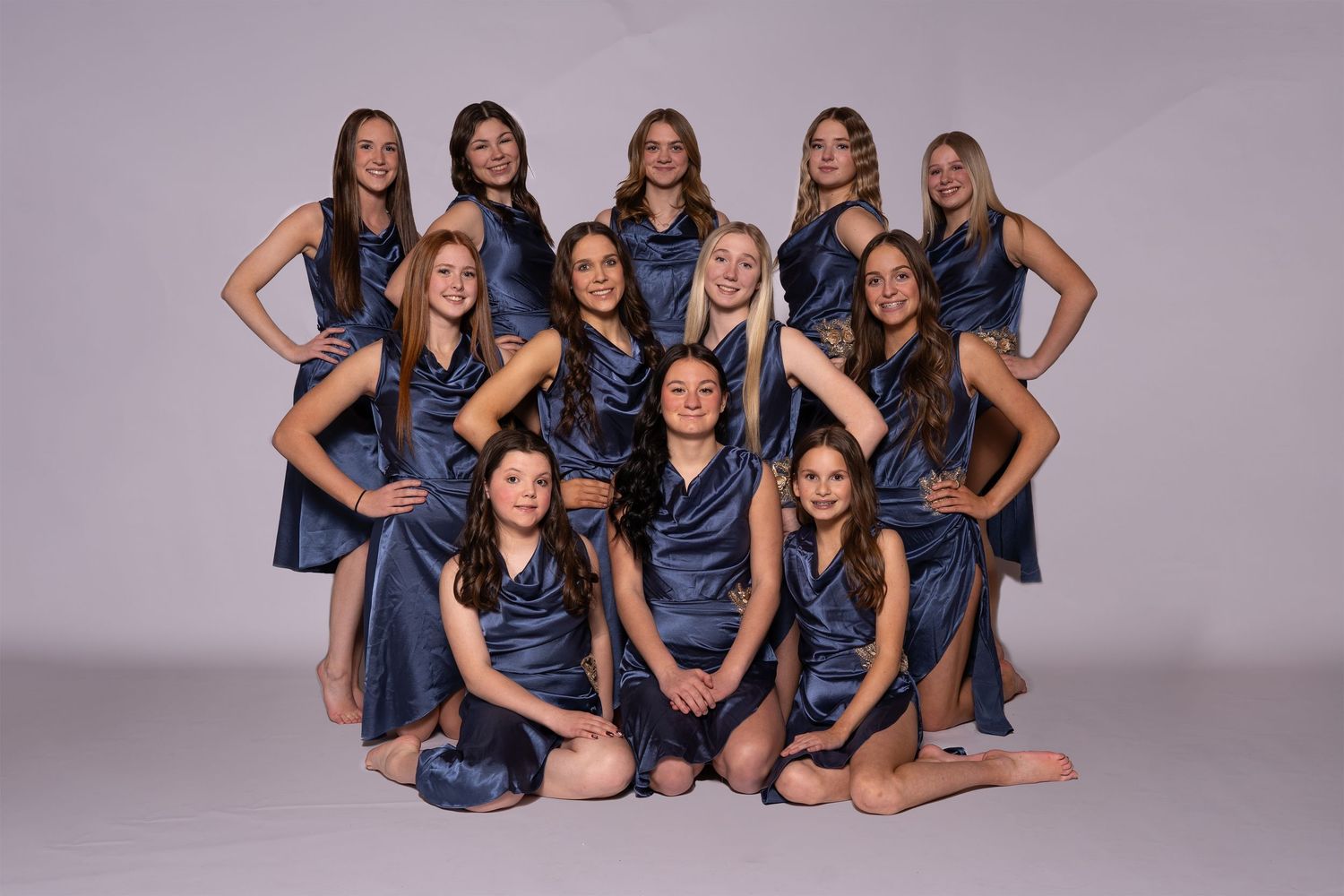 Dance team members wearing matching navy blue dresses pose together in various formations.