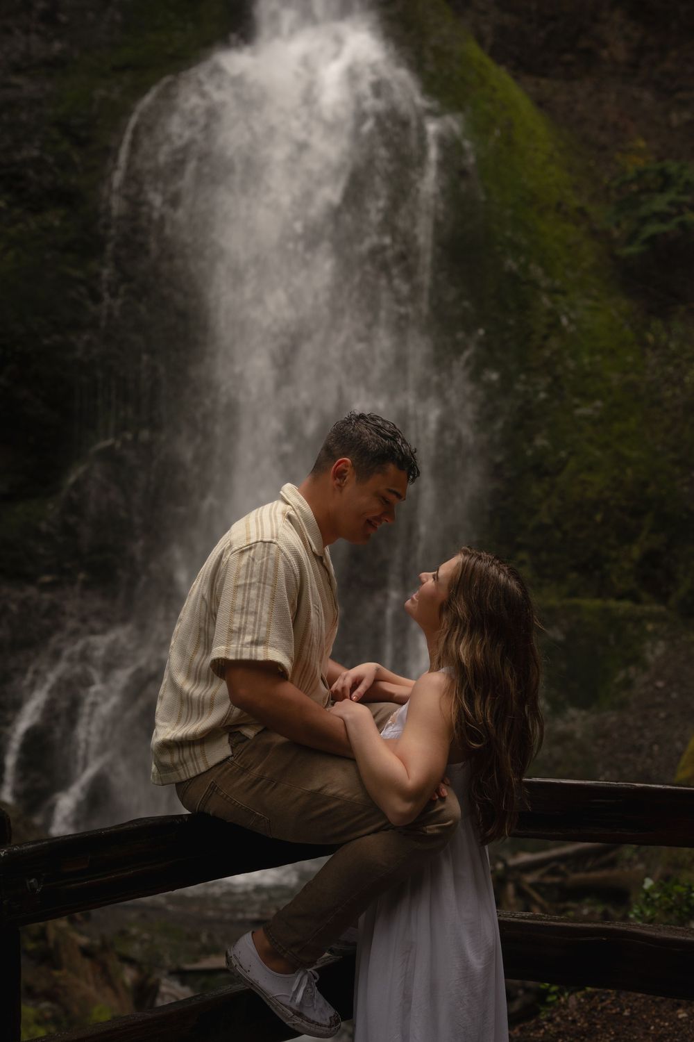 A cascading waterfall forms a dramatic backdrop behind a wooden observation deck in a misty forest setting.