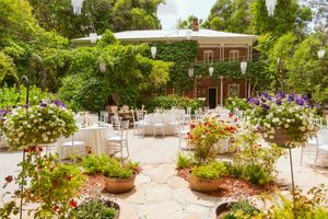 Beautiful outdoor patio dining area surrounded by colorful potted flowers and greenery in an elegant garden setting.