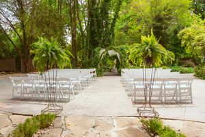 White folding chairs set up for an outdoor garden wedding ceremony surrounded by lush tropical plants and palm trees.