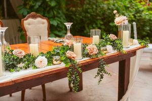 A rustic wooden table decorated with floral arrangements, candles, and glassware for an elegant outdoor event setting.