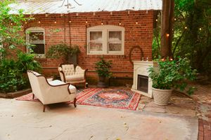 A cozy brick patio seating area featuring vintage chairs, a Persian rug, and white fireplace against exposed brick walls.