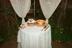 Wedding dessert table with two cakes displayed on a white lace tablecloth with sheer draping.