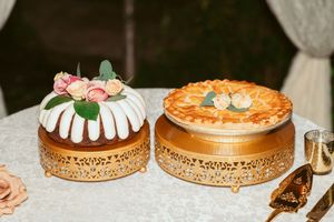 Two elegant desserts displayed on ornate gold cake stands including a bundt cake with flowers and decorated pie.