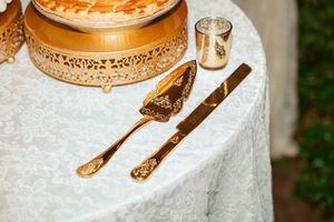 Ornate gold-plated cake serving set with knife and server placed on white lace tablecloth.