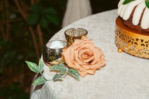 Close-up of wedding table decor featuring a peach rose, tea light holders, and gold cake stand details.
