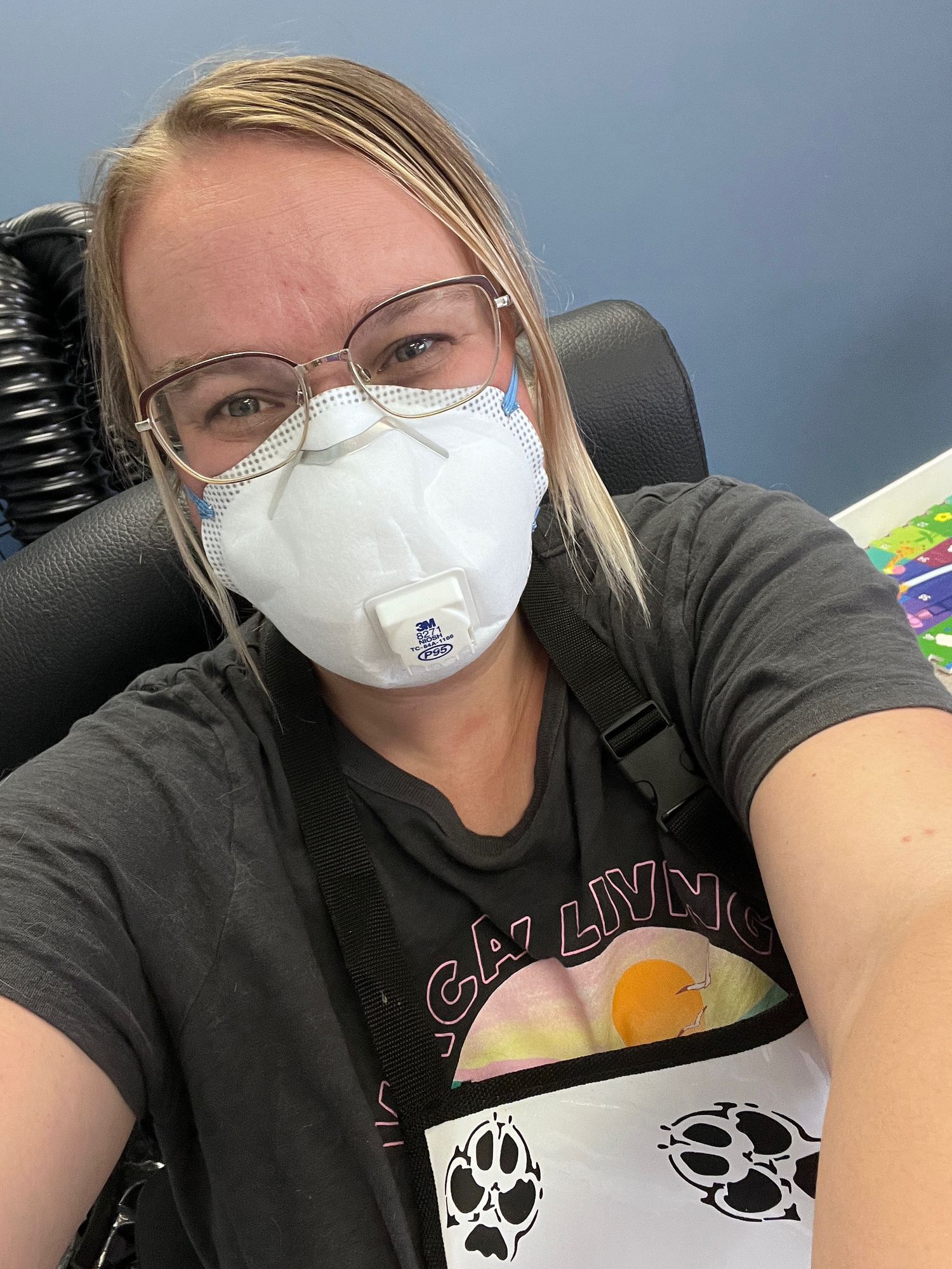 Healthcare worker wearing N95 mask takes selfie while sitting in car wearing graphic t-shirt with paw prints.