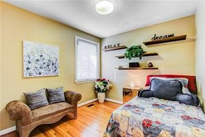 Cozy bedroom with yellow walls, brown chaise lounge, hardwood floors, and decorative wall shelves with plants.