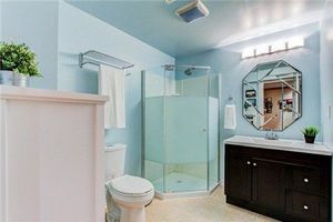 Spacious modern bathroom with glass shower enclosure, relaxing light blue walls, and dark wood vanity.