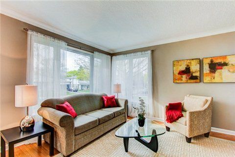 Modern living room with sofa, red accent pillows, and beige walls featuring abstract artwork.