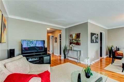 Contemporary living area with large TV, grey sofa, and red accent pillows on hardwood flooring.