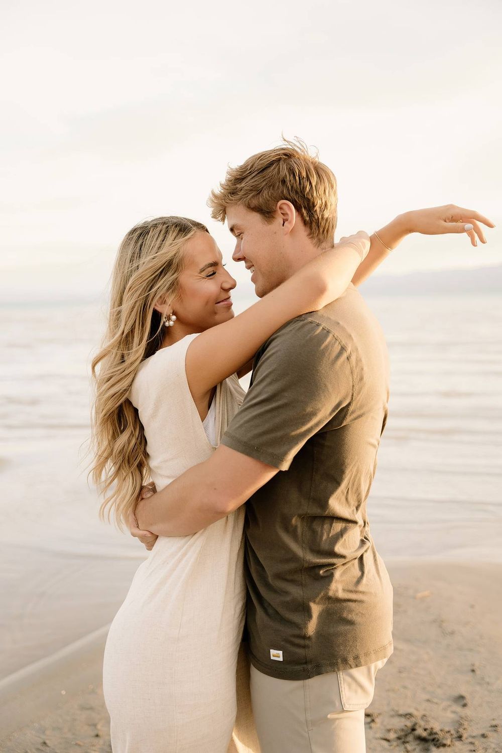 Intimate moment between couple embracing on beach with ocean horizon in warm lighting.