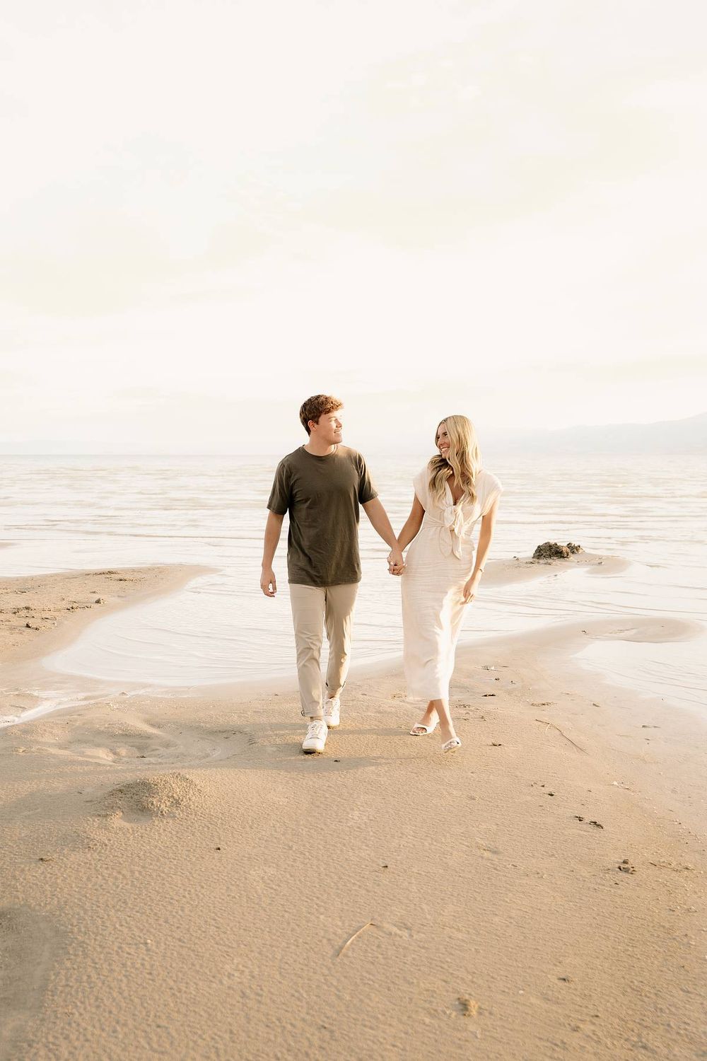 Couple walking hand in hand along peaceful beach shoreline at sunset.