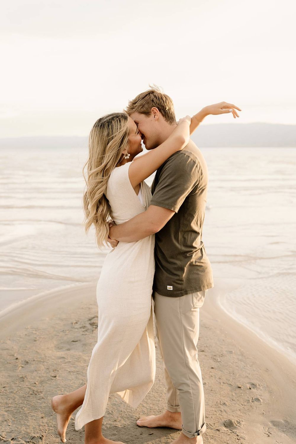 Intimate couple sharing a tender moment on windswept beach at golden hour.