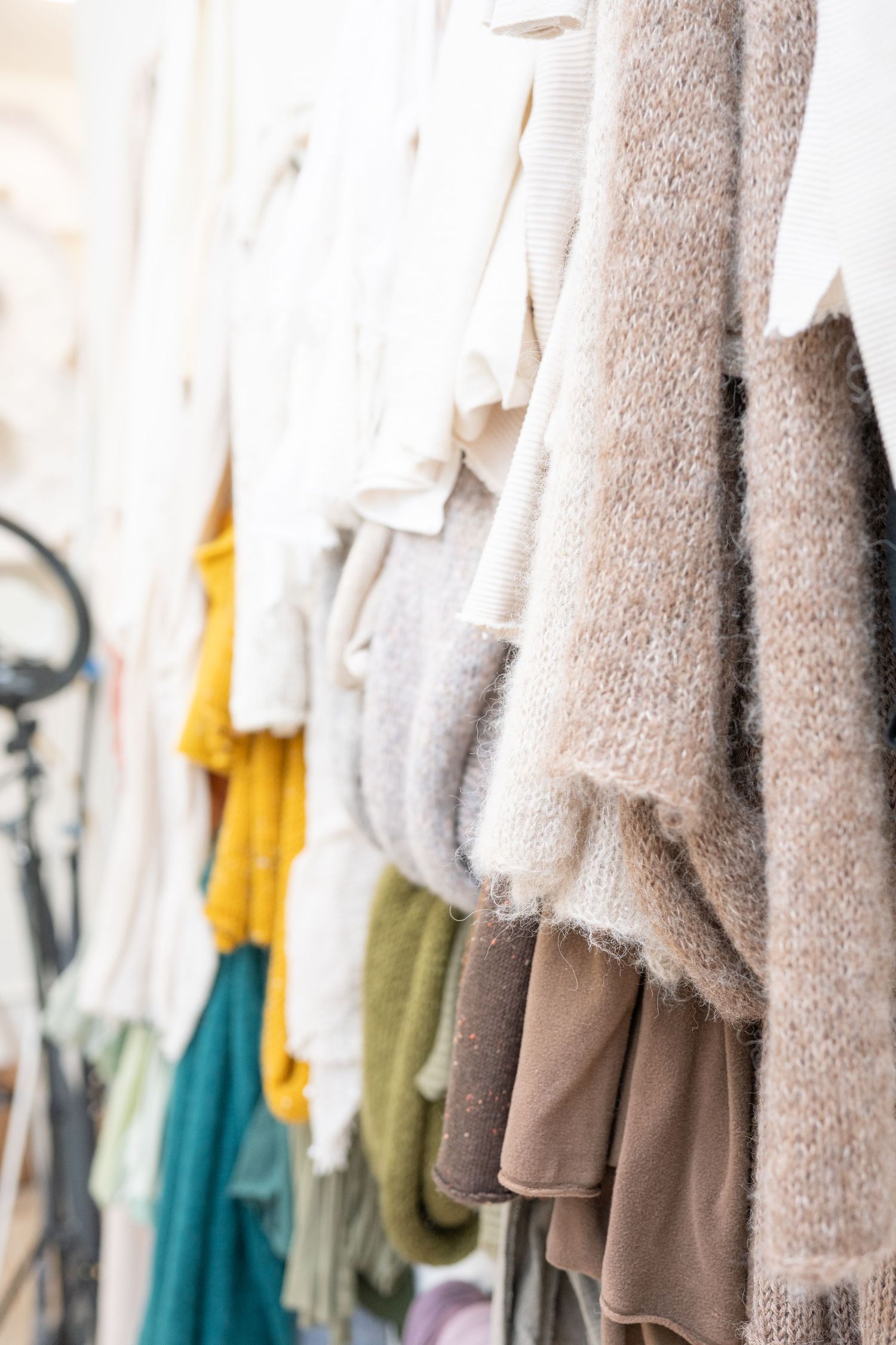 Close-up view of cozy knit sweaters in neutral and bright colors hanging on wall.