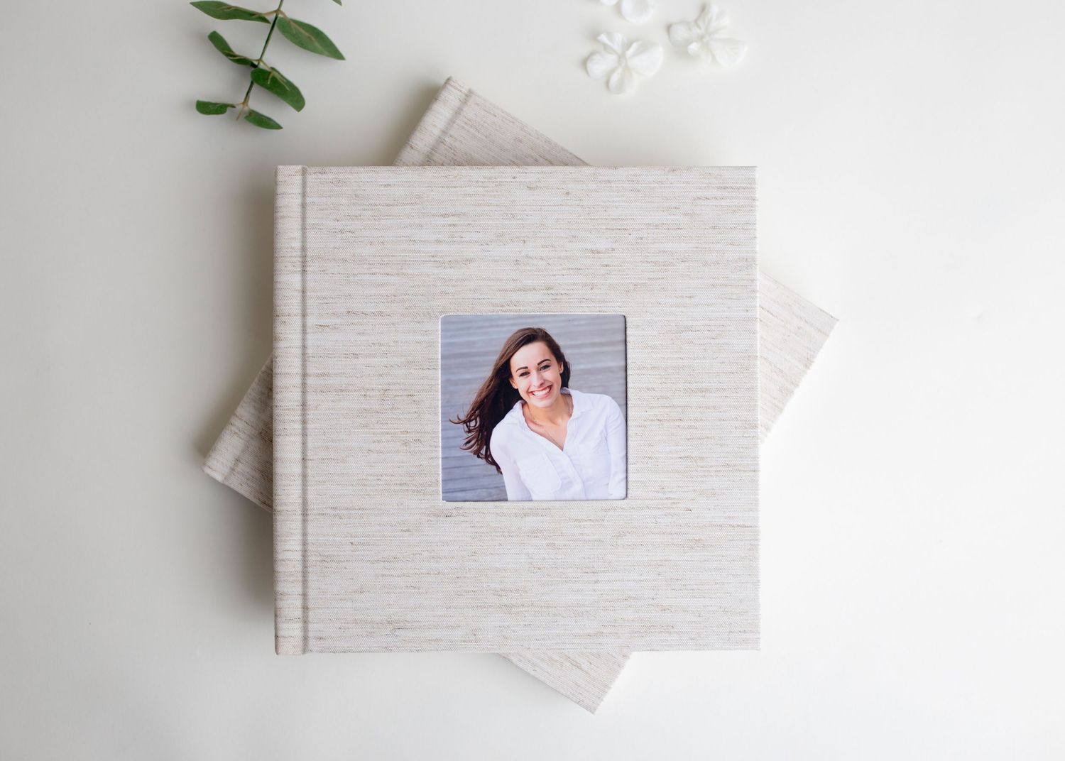 Elegant linen photo albums with delicate green foliage accents displayed on white surface.