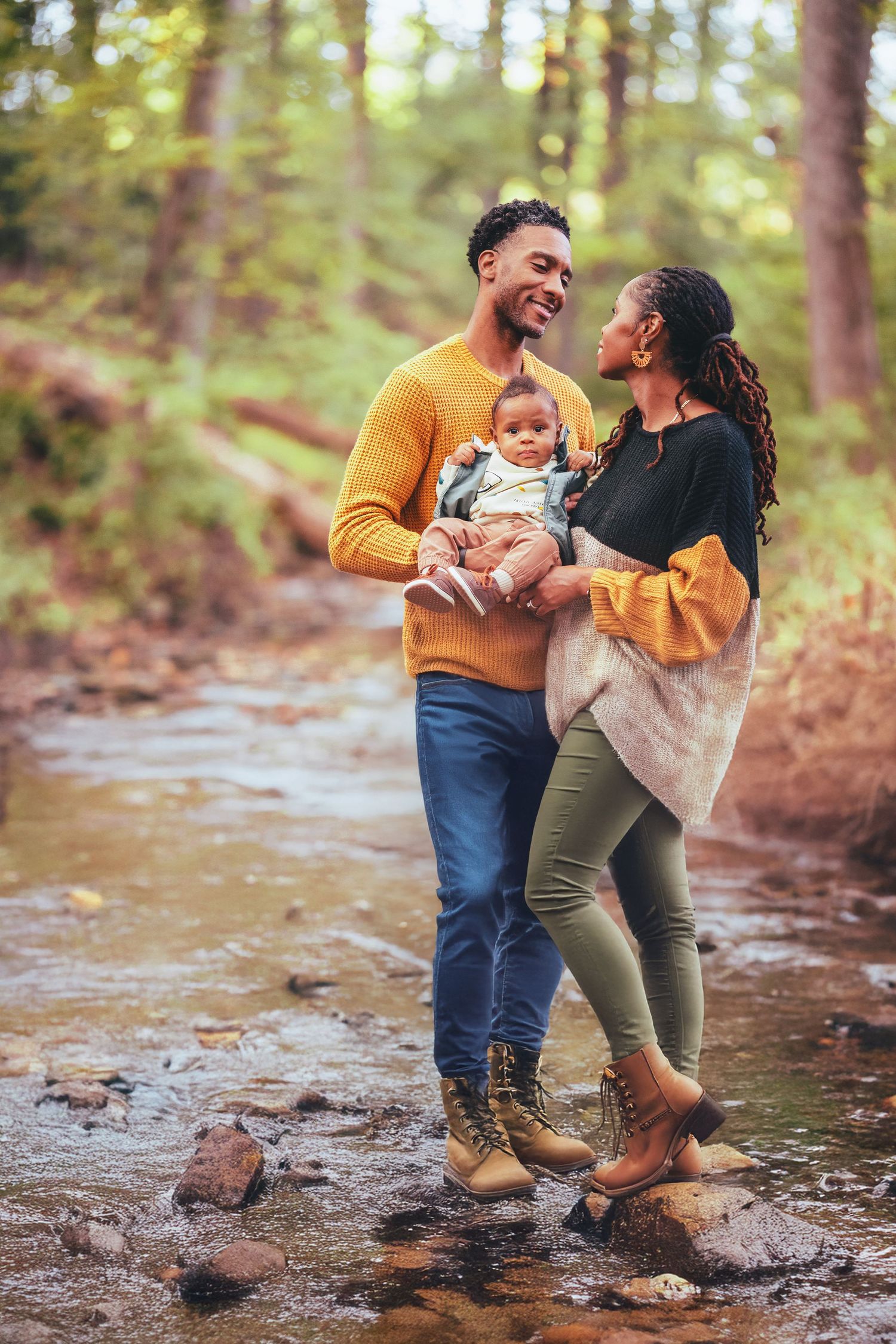 A happy family enjoying quality time together while standing on rocks near a stream in a wooded forest setting in Rockville, MD.