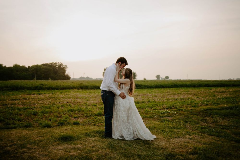 A romantic wedding photoshoot in a golden field at sunset with flowing white dress details.