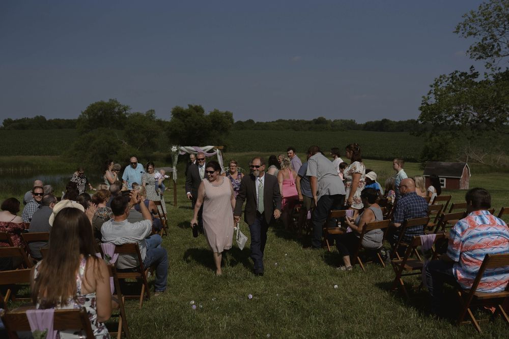Outdoor wedding reception setup with tables and chairs on a grassy field.