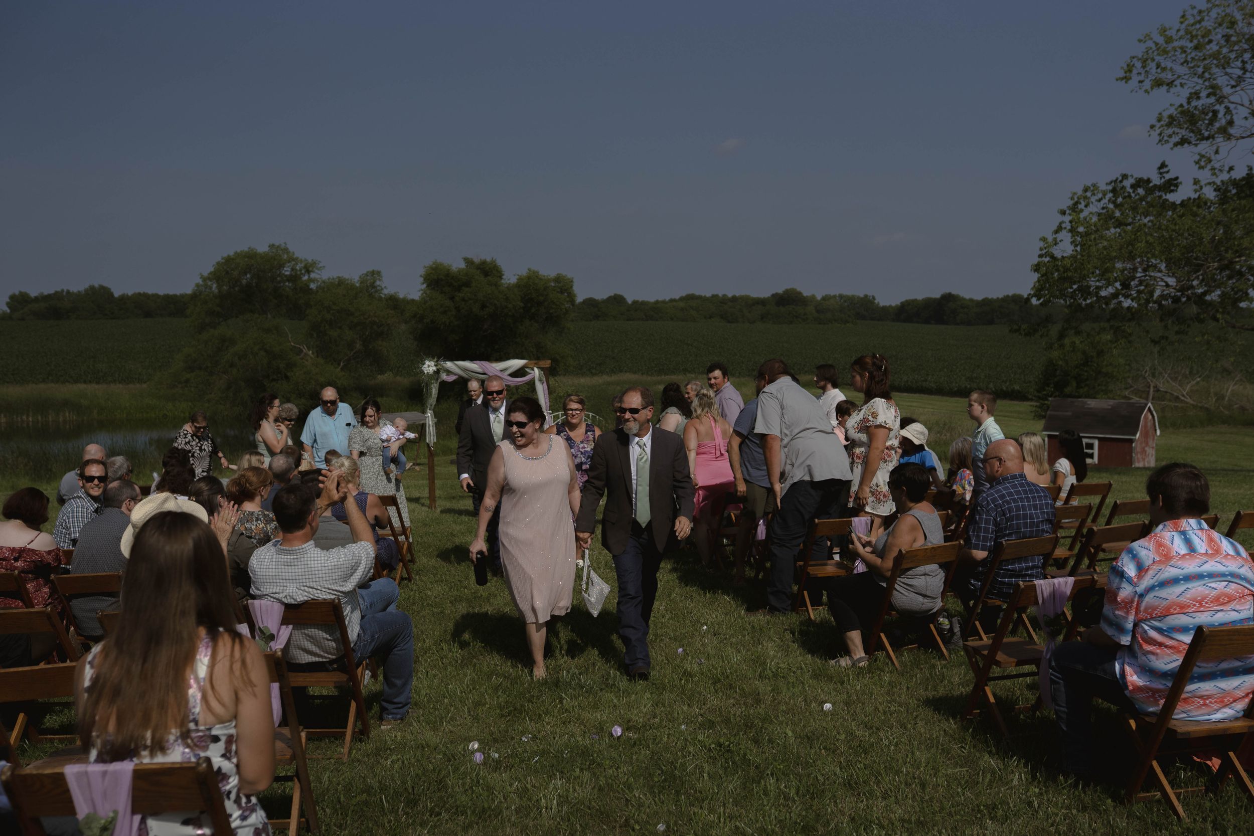 Outdoor wedding reception setup with tables and chairs on a grassy field.