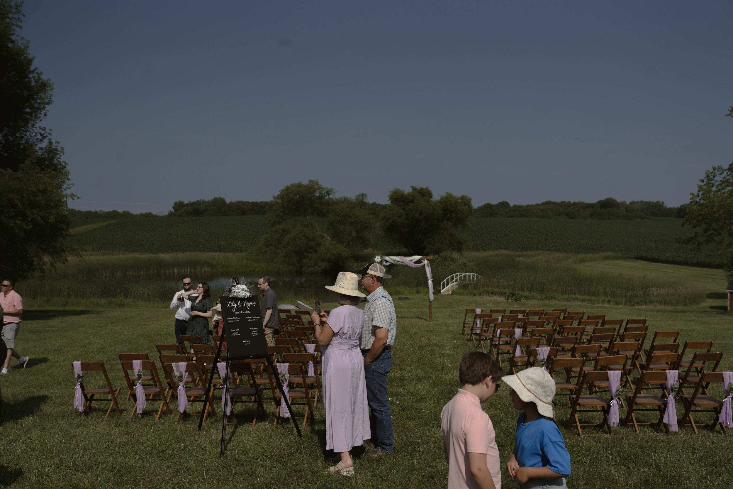 Rustic outdoor wedding ceremony setup with wooden chairs arranged in rows on a grassy field.