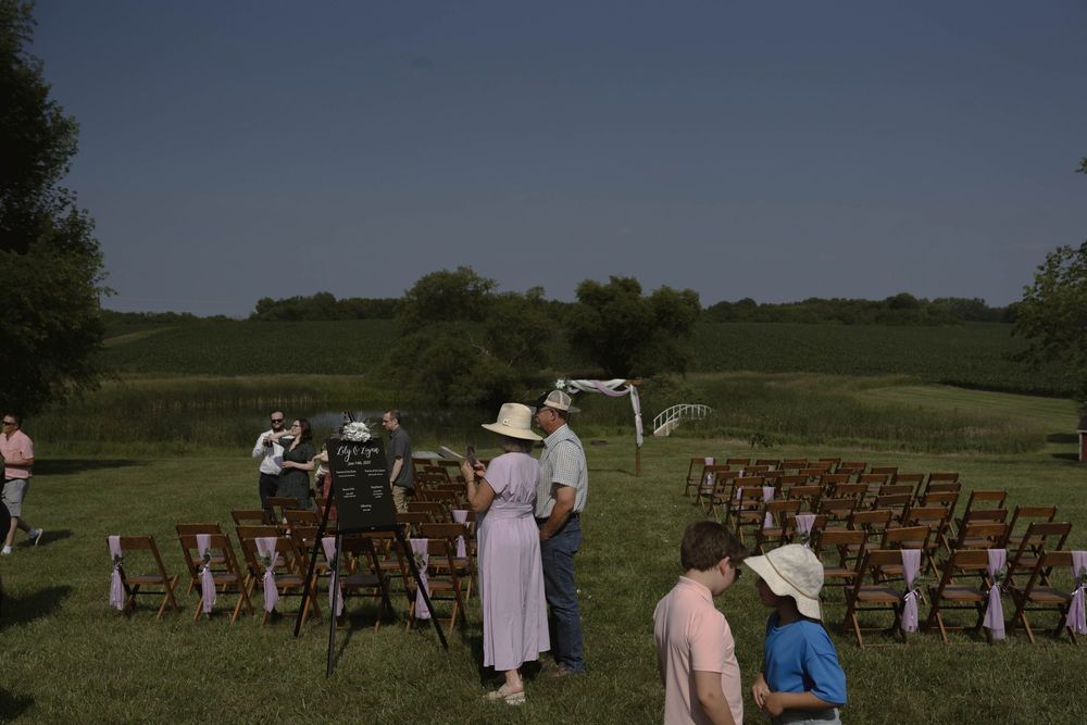 Rustic outdoor wedding ceremony setup with wooden chairs arranged in rows on a grassy field.