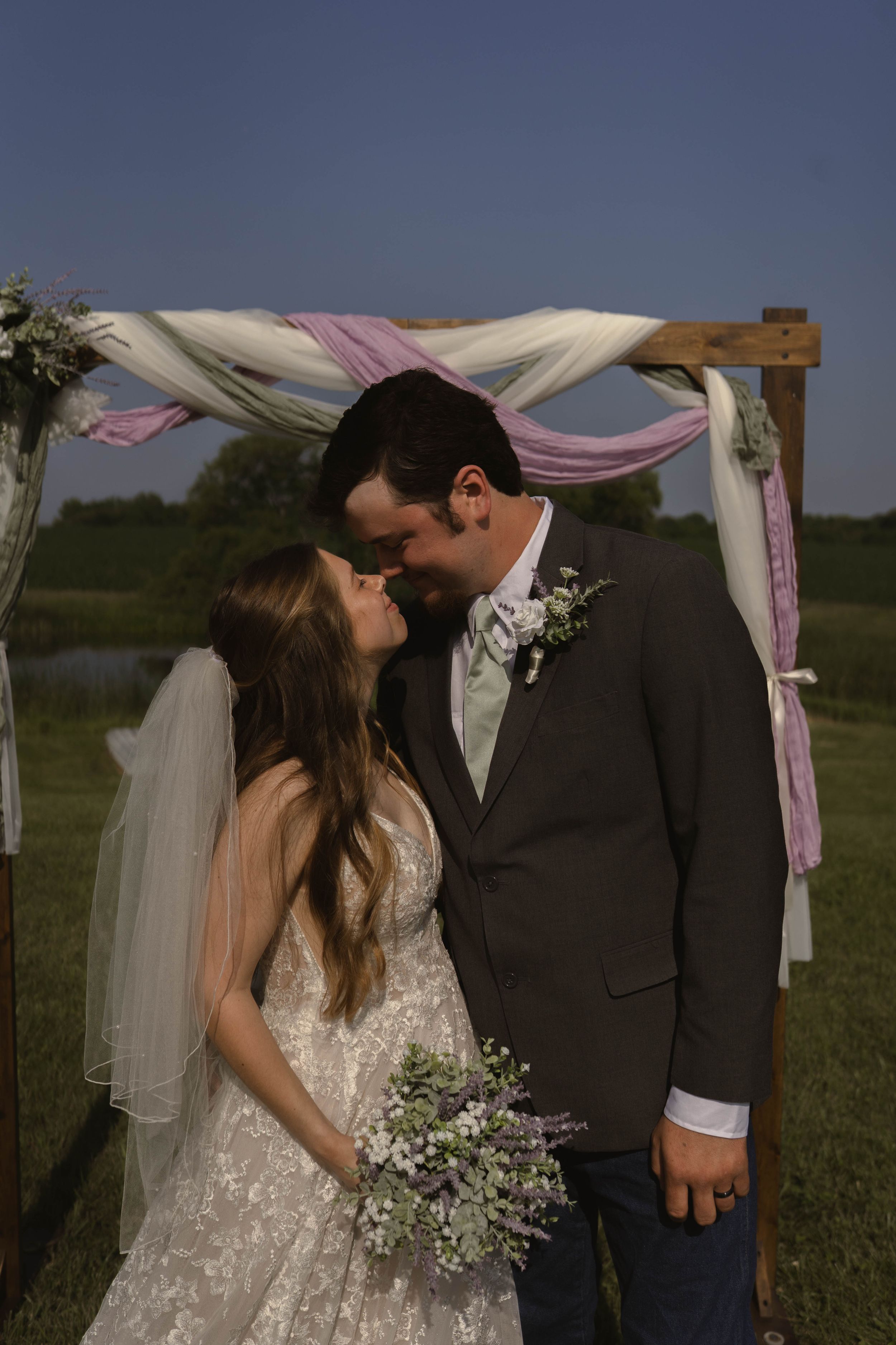 Romantic outdoor wedding ceremony under a draped arch with pink and white fabric.