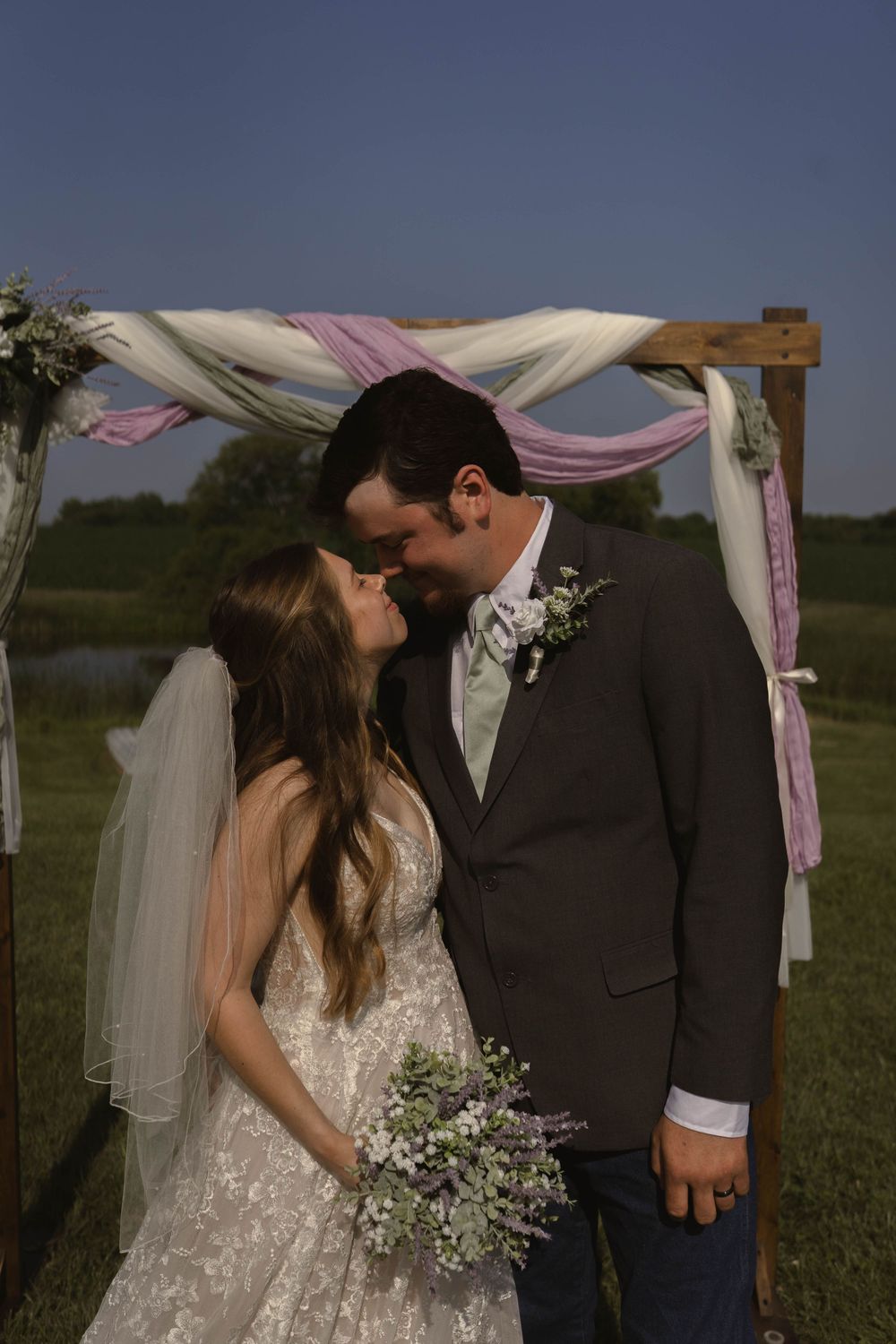 Romantic outdoor wedding ceremony under a draped arch with pink and white fabric.