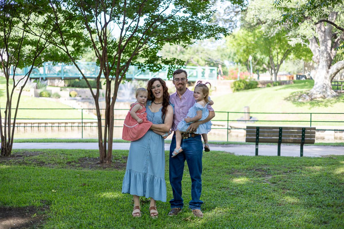 Family members walk together through a lush park setting on a sunny summer day.