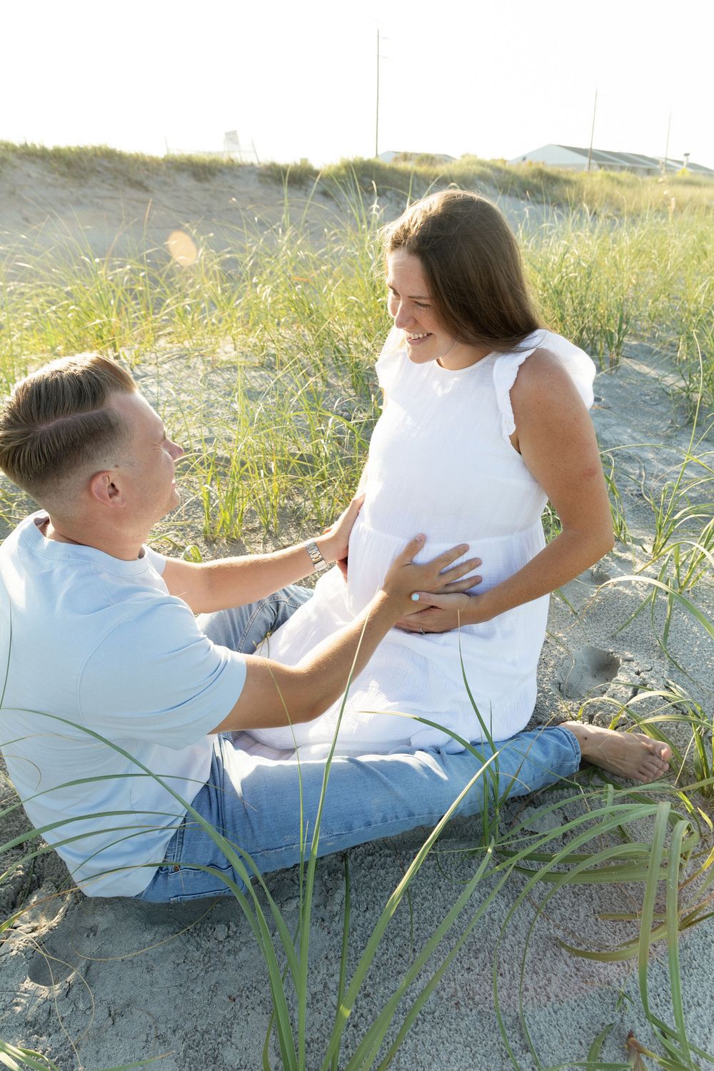 Man sitting on sandy beach touching pregnant womans belly, sharing tender moment together.