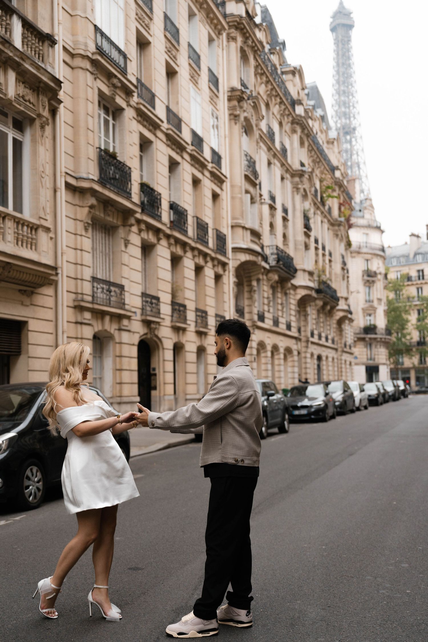 A romantic scene on a classic Parisian street with the Eiffel Tower visible in the background through elegant buildings.