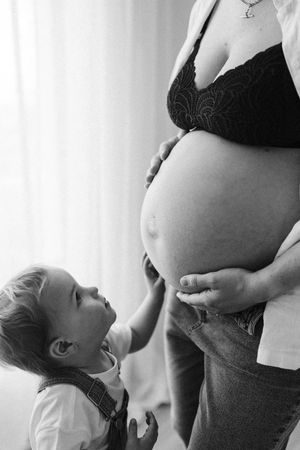 Black and white photo of toddler touching mother's pregnant belly with curiosity.