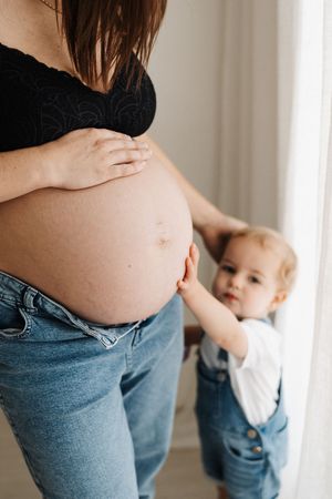 Young toddler reaches up to touch mother's pregnant belly in candid moment.