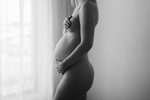 Silhouette of pregnant woman standing by window in black and white.