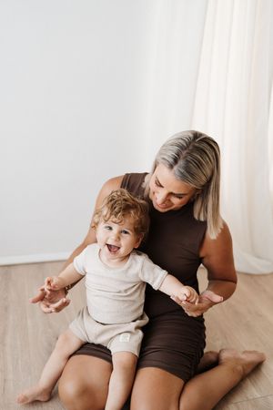 Playful interaction on wooden floor against white curtains showing genuine laughter.