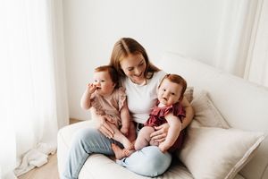 Mother sitting on couch embracing two babies in coordinating outfits.