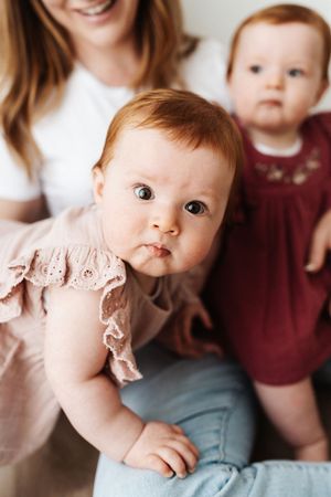 Close-up portrait of infants in pink and burgundy dresses sitting together in a bright room.
