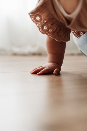 Close-up of a tiny hand and lace dress detail touching a wooden floor.
