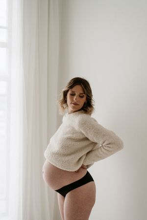 Maternity photo of woman in cream sweater and black underwear.