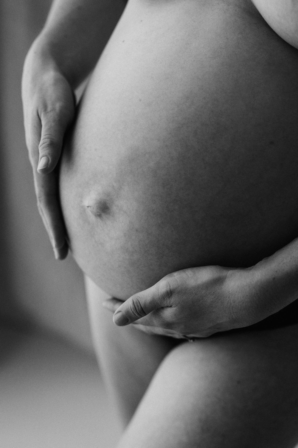 Black and white close-up of hands cradling pregnant belly.