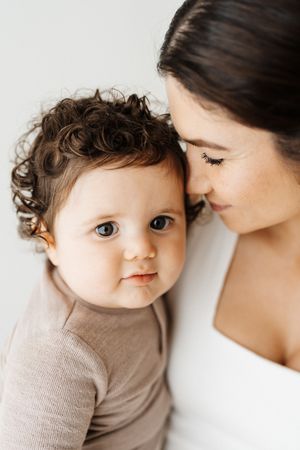 Close-up portrait of baby with curly hair and parent against white background.