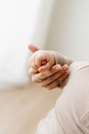 Close-up of tiny baby hand gently held in adult hand with soft natural lighting.