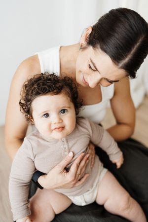 Tender moment between parent and baby in beige outfit sitting together indoors.