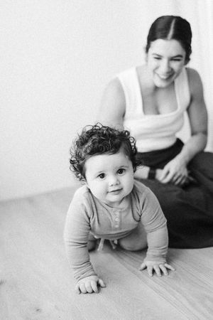 Black and white portrait of happy baby with curly hair and parent in casual attire.