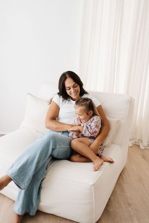 Mother and child sharing intimate moment while relaxing on white couch.