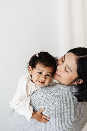 Smiling baby in white sweater cuddling with parent wearing grey knit sweater.