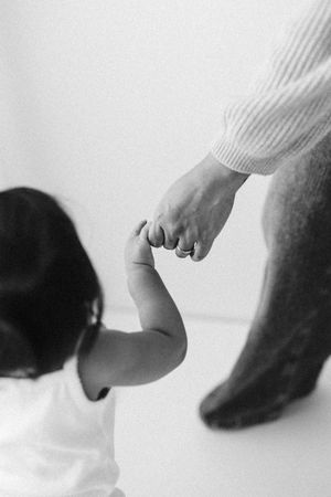 Black and white image of small child reaching up to hold parent's hand.